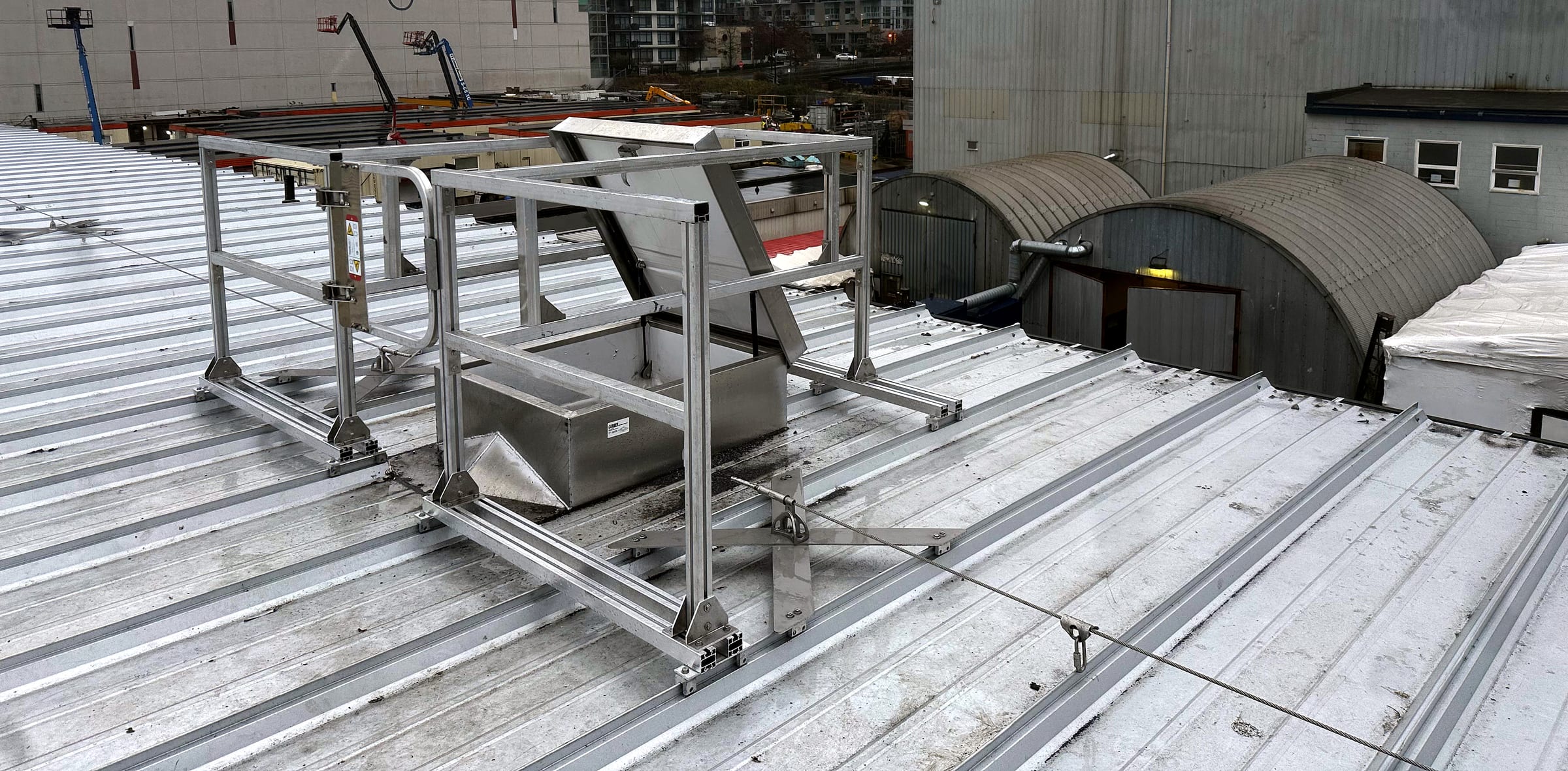 Aluminum guardrail enclosure with a gate around an open roof hatch on a metal roof.