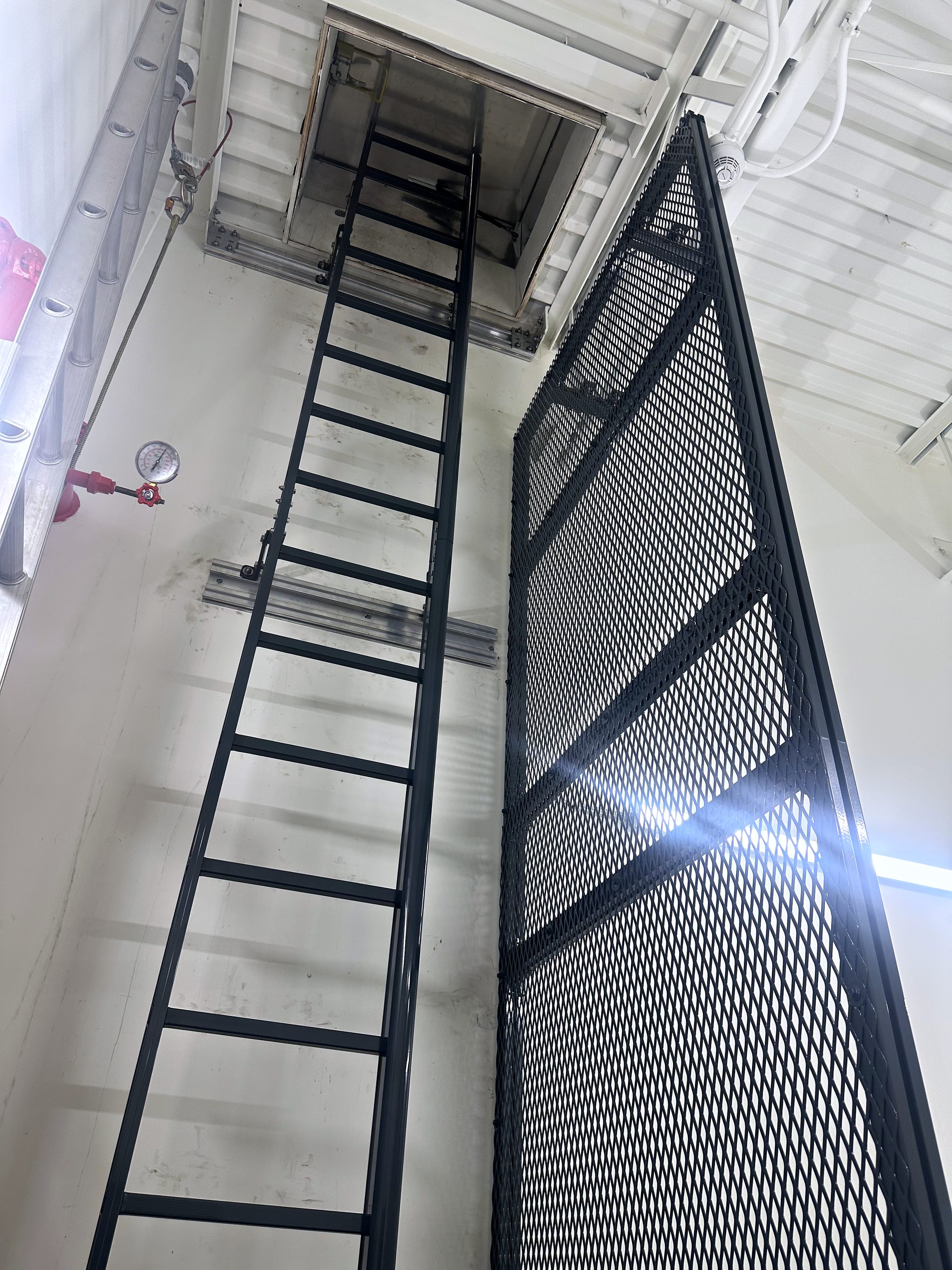 Fixed ladder in a safety cage leading up to an open roof hatch.