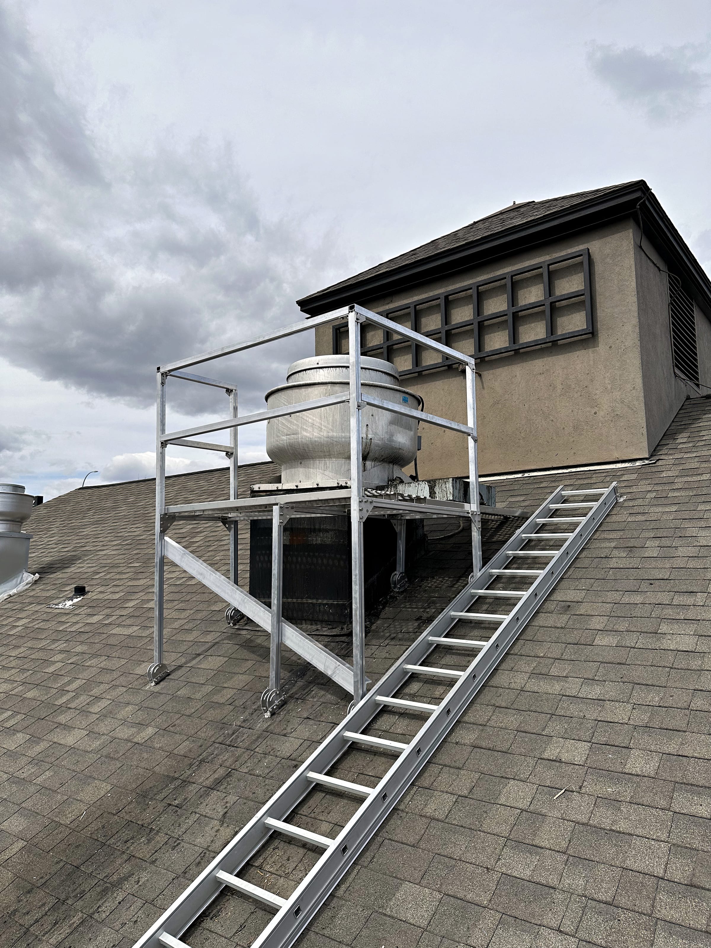 Braced aluminum guardrail cage around rooftop equipment, with an access ladder.